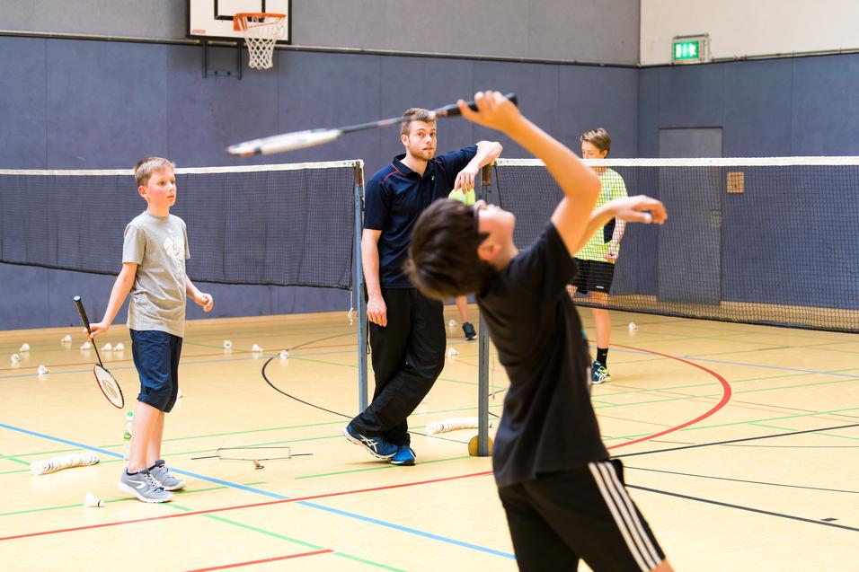 Gruppentraining im Badminton: Kinder üben mit Schlägern und Bällen unter Anleitung eines Trainers in einer Sporthalle.